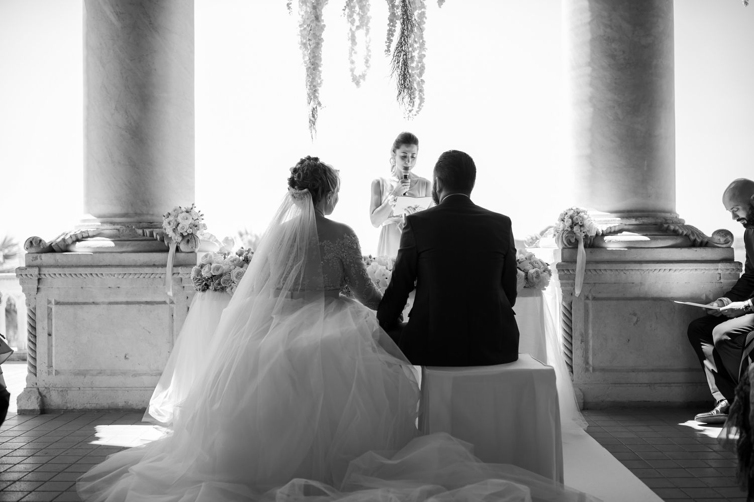 A minimalist black and white photo of a wedding ceremony through architectural columns.