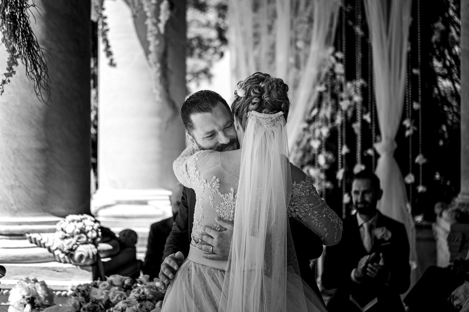 Wedding ceremony in columned venue with dramatic lighting and hanging decorations.