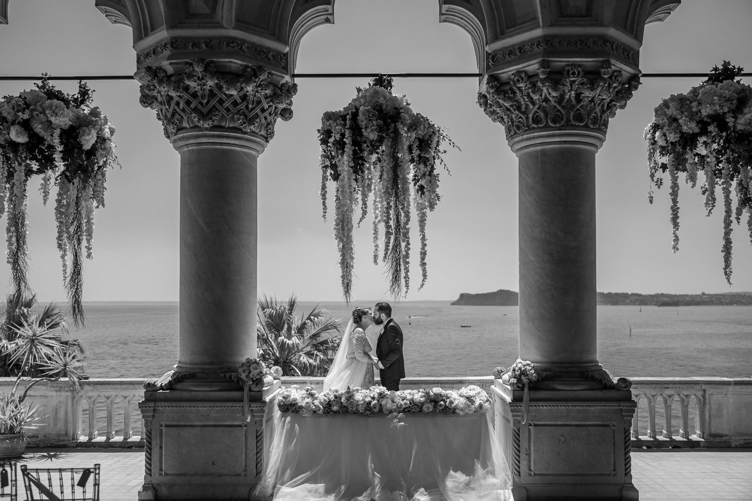 Wedding ceremony setup with classical columns and hanging floral decorations in natural light.