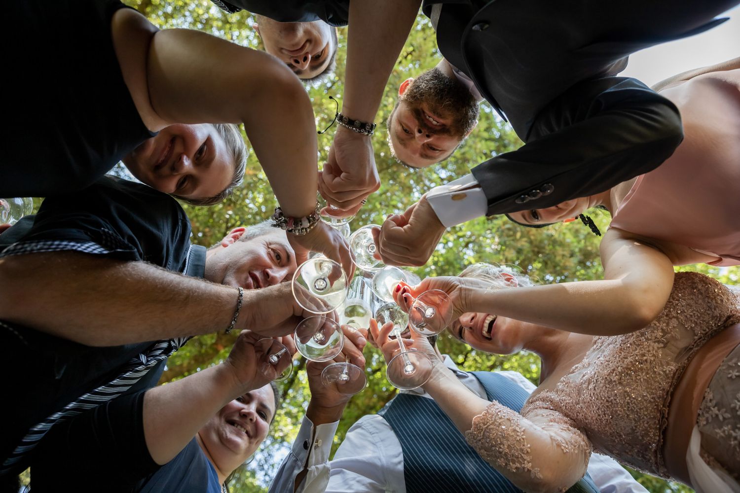 Close-up of champagne toast with multiple hands holding glasses in outdoor setting.