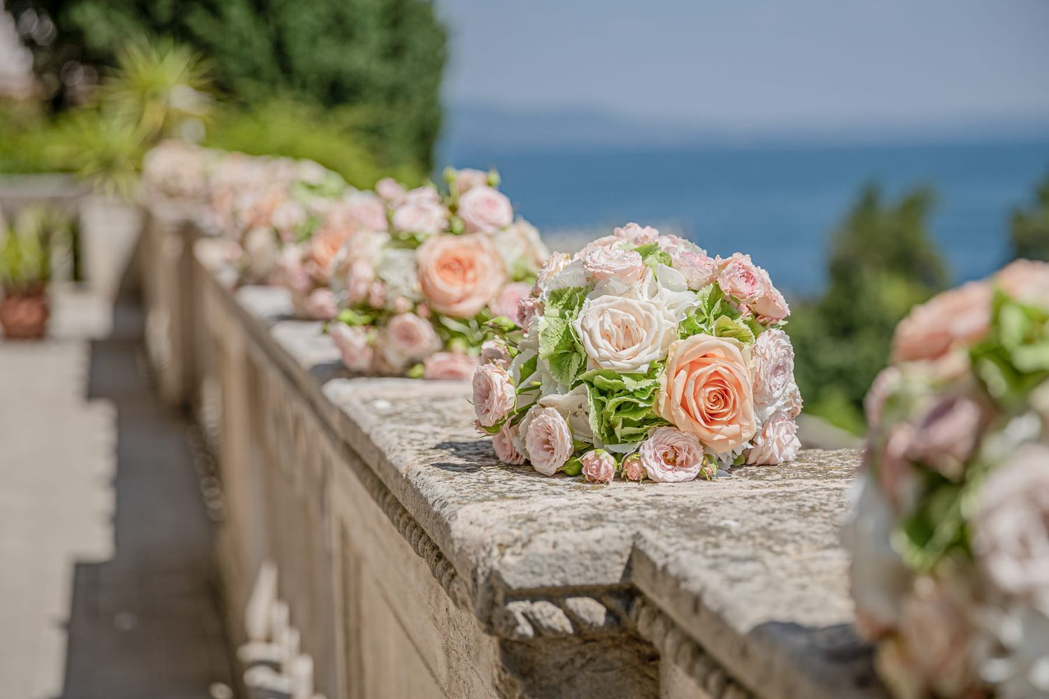Delicate pink and peach floral arrangements adorning stone balustrade with ocean view.