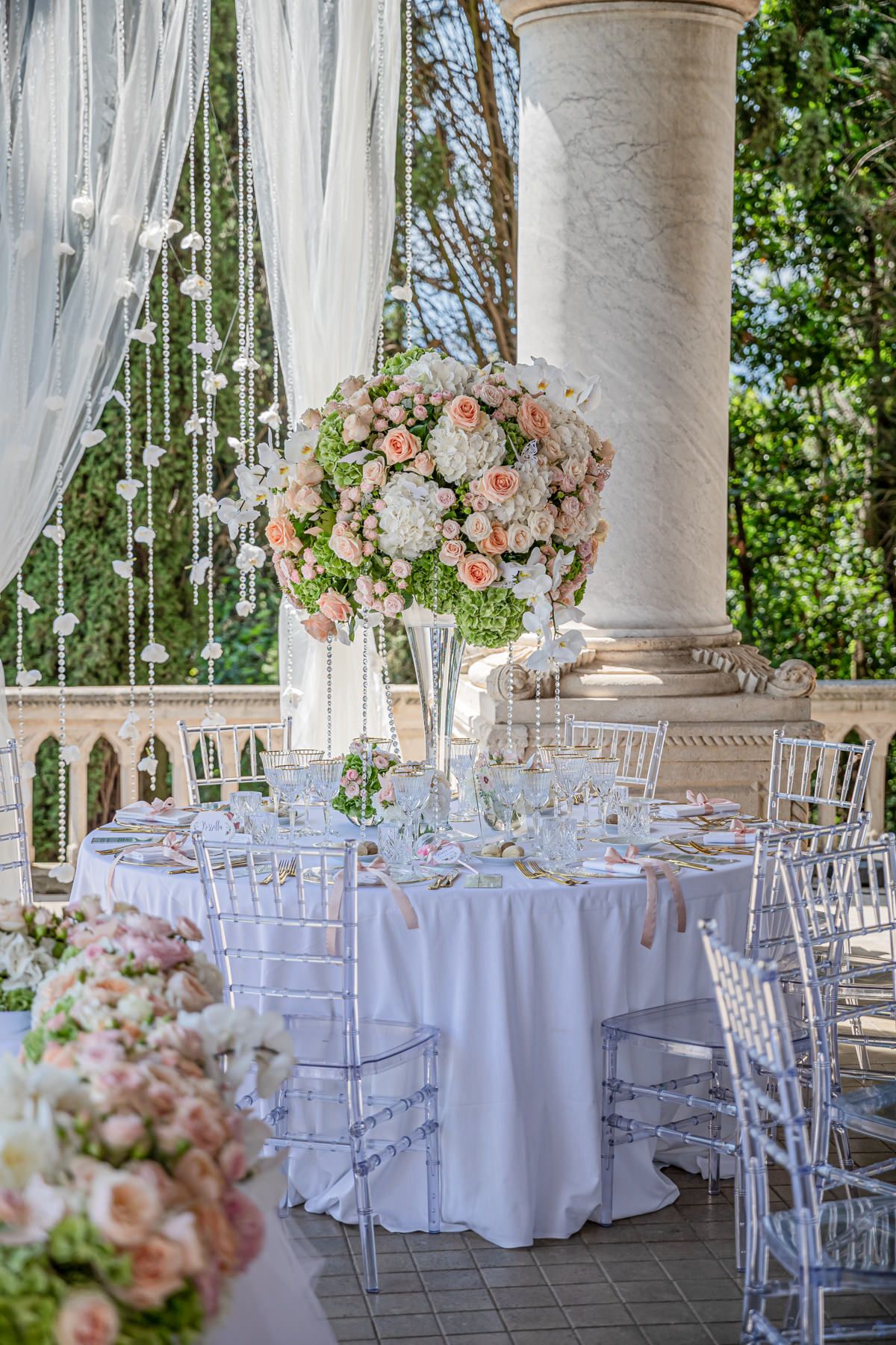 Elegant wedding reception setup with white drapes, columns and pink floral centerpieces.