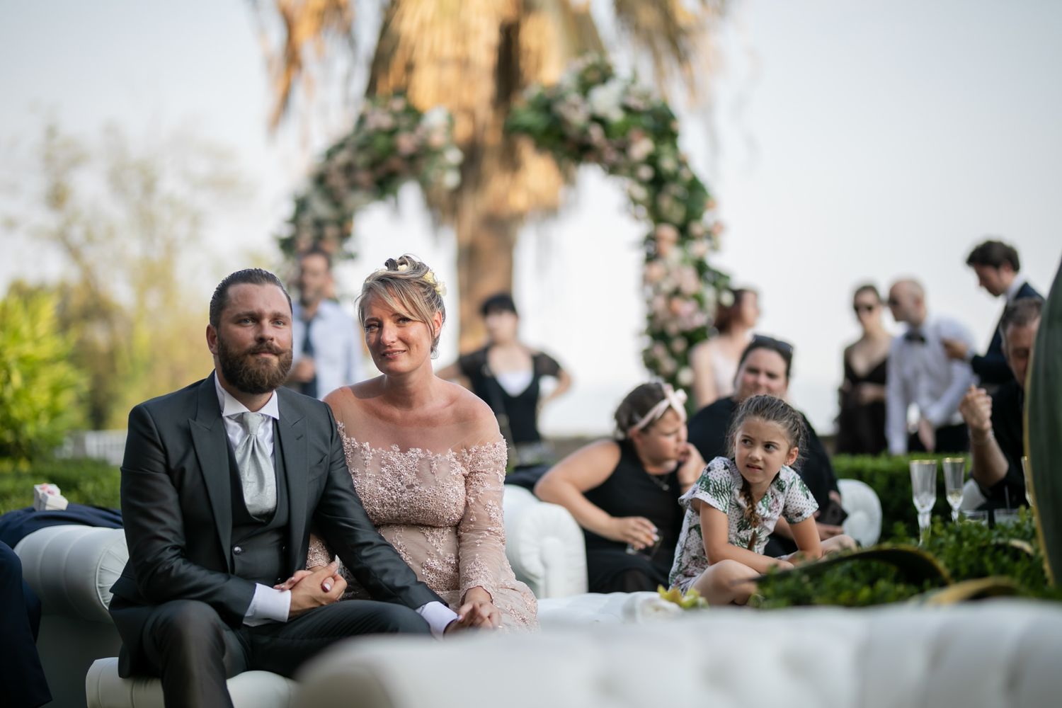 Outdoor wedding reception with guests seated under floral decorations.