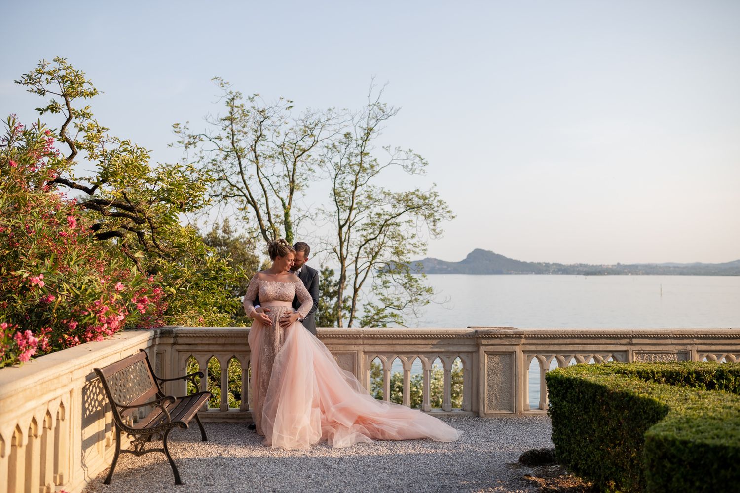 Elegant wedding couple poses on a stone terrace overlooking a scenic coastal view.