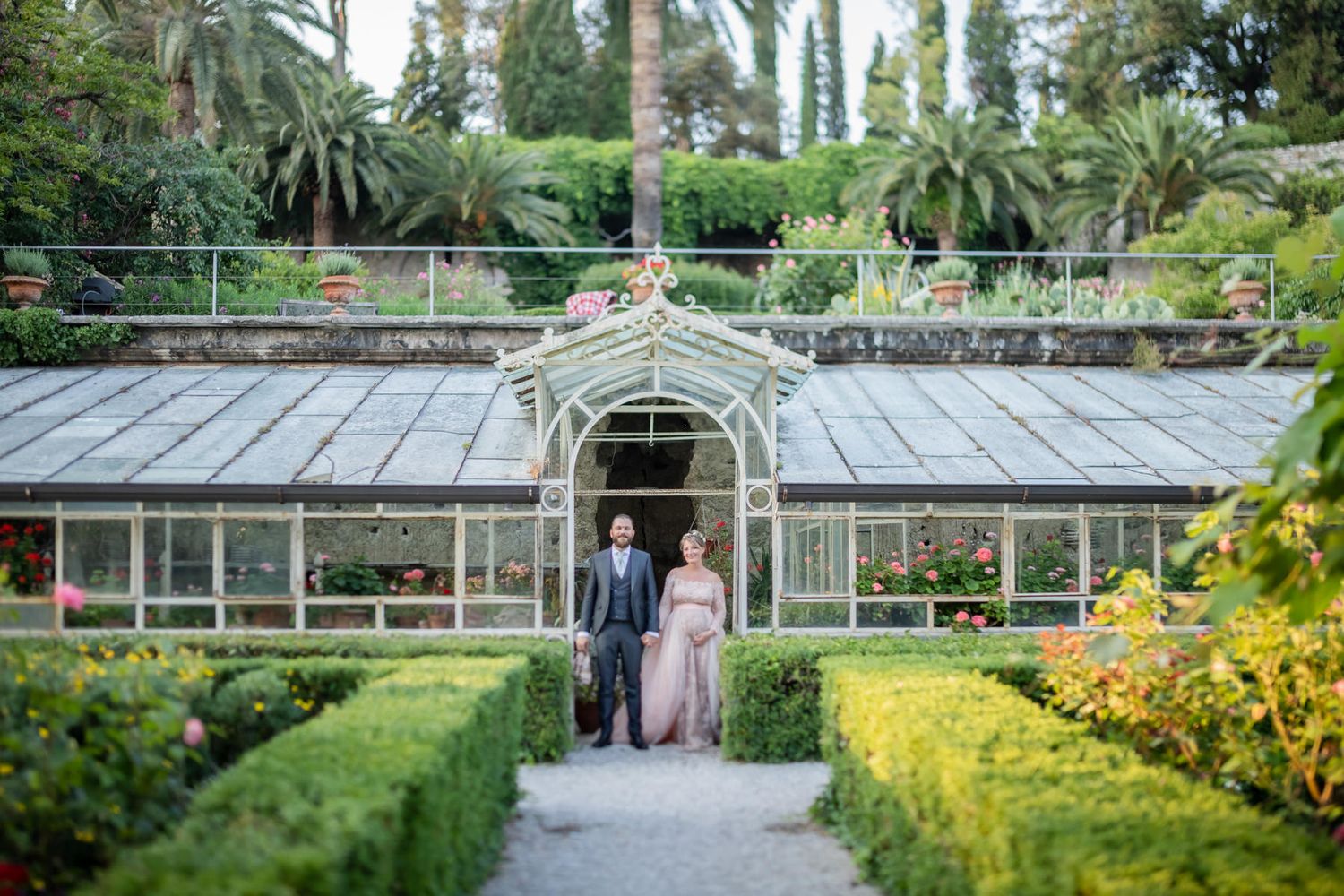 Wedding couple poses in front of a vintage greenhouse with tropical garden landscaping.