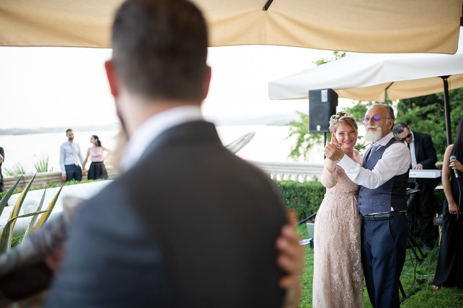 Wedding celebration under a white tent canopy with guests mingling in formal attire.