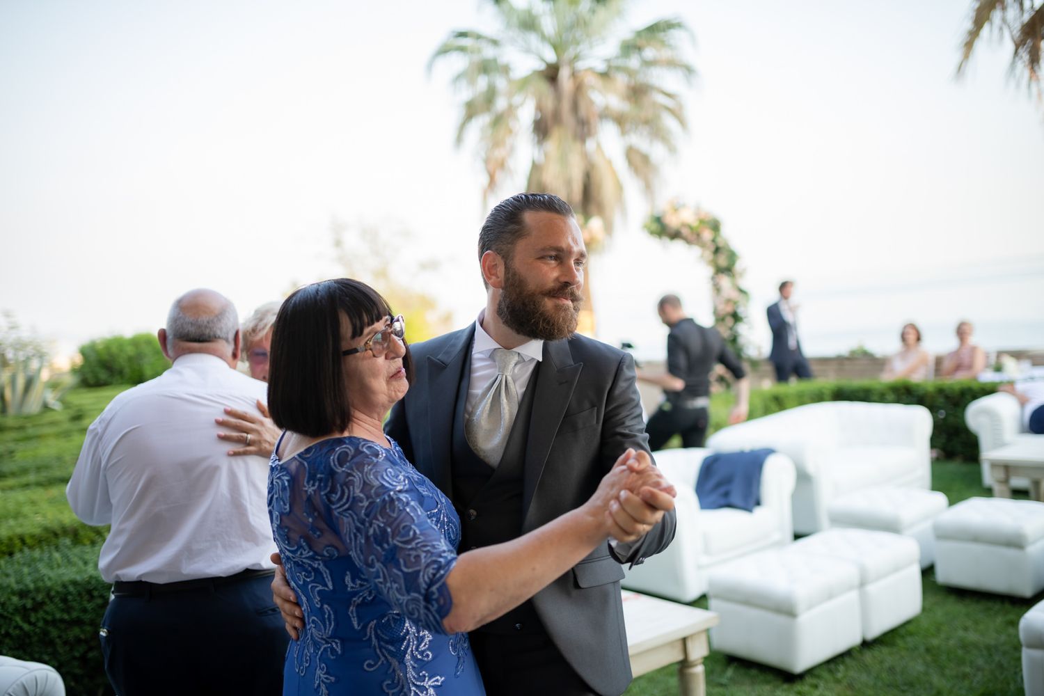 Outdoor wedding reception with palm trees and white lounge furniture setup.