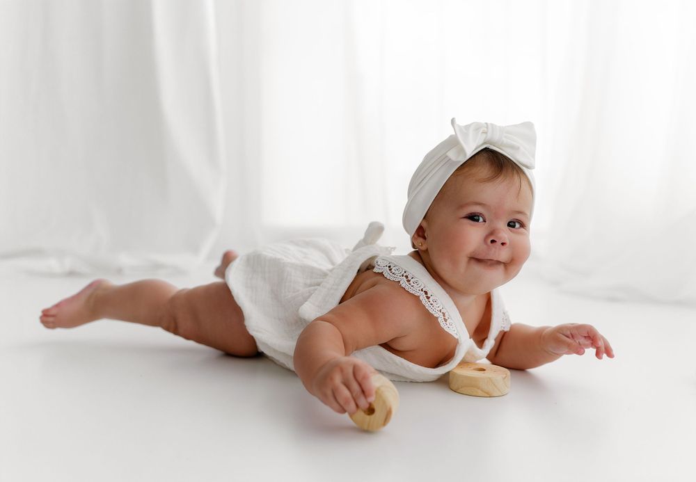 Baby wearing white romper crawls on white background during studio photography session.