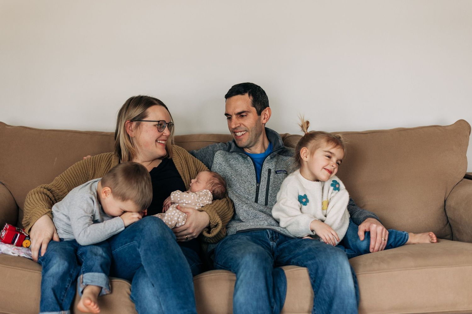 Family lounging together on tan couch sharing intimate moments with young children.