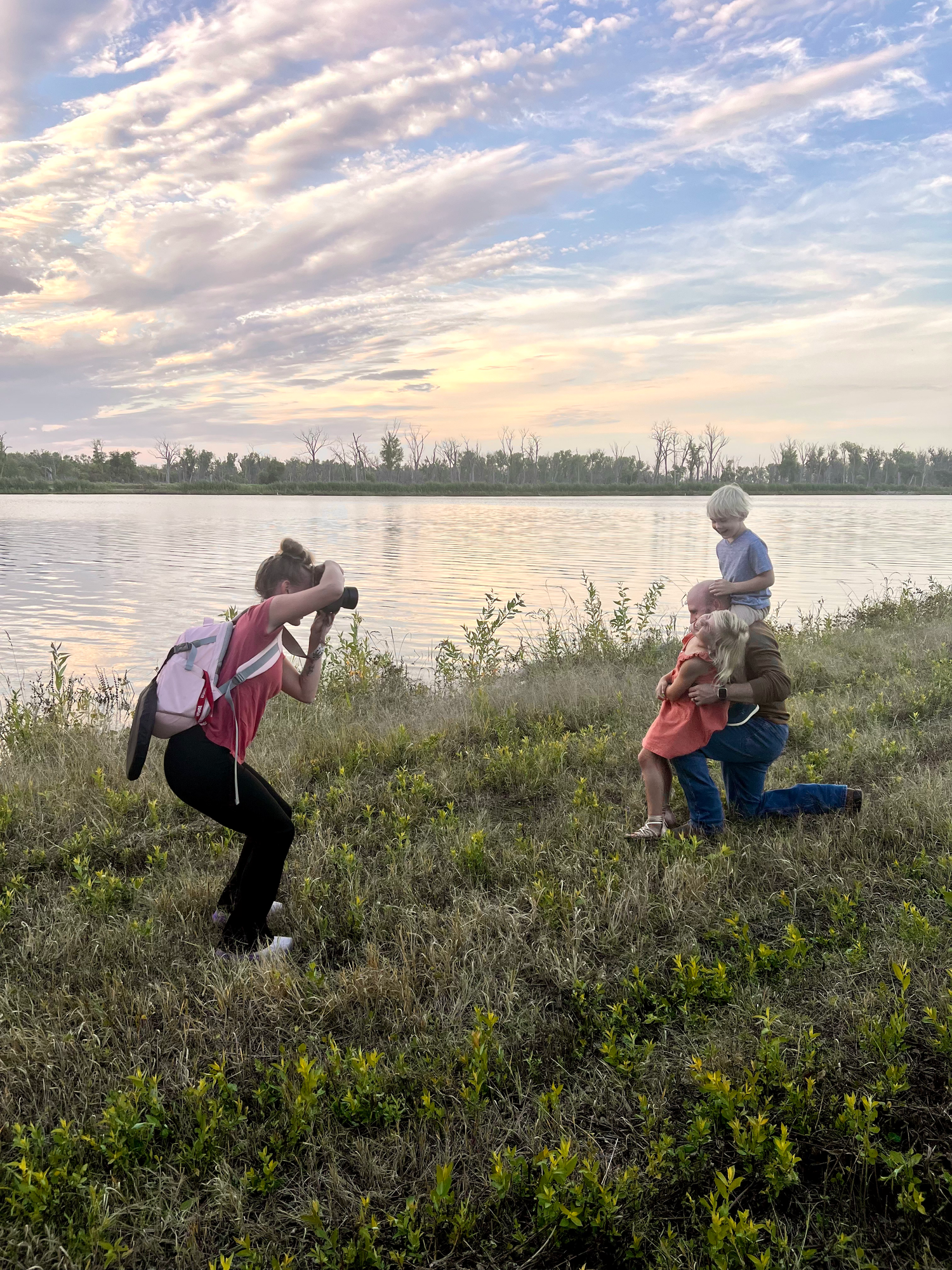 Photographer capturing family photos during golden hour by a serene lake.