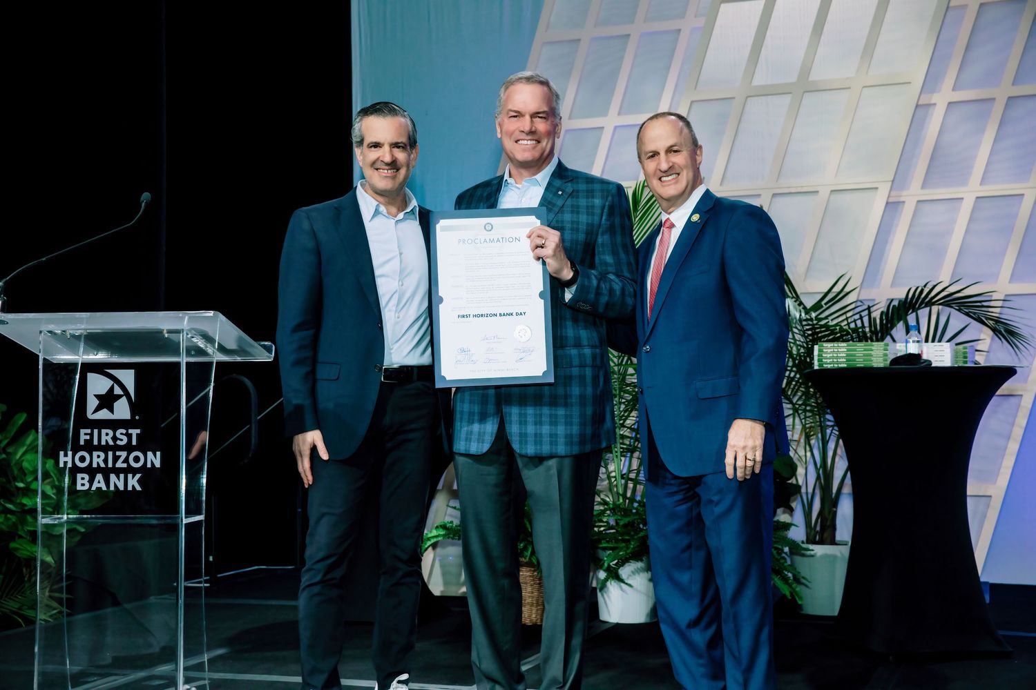 Business professionals in suits stand together holding awards and certificates during a corporate ceremony.