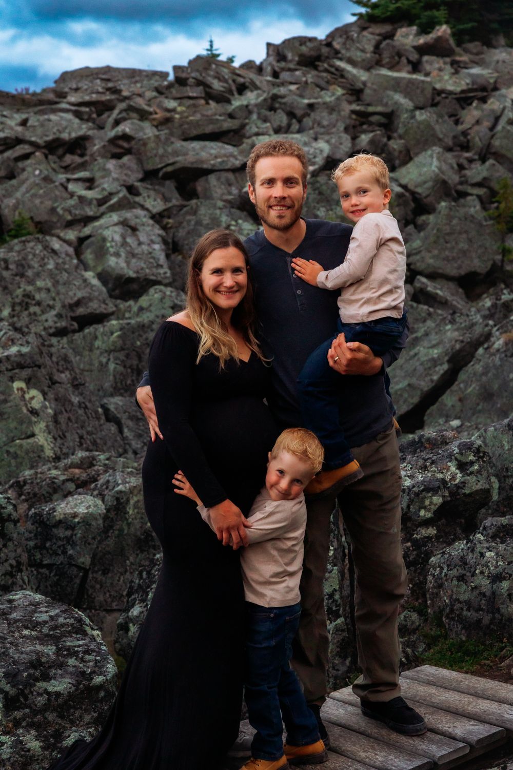 Family portrait on rocky outcrop with expecting mother in black dress and two young children.