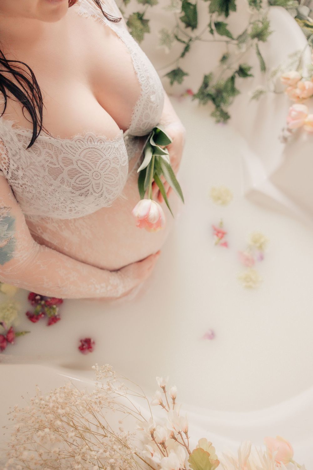 Delicate maternity boudoir scene with pink flowers and white lace.