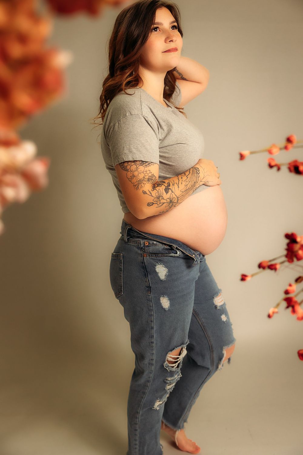 A figure in ripped jeans and gray t-shirt poses artistically against a beige background with red floral accents.