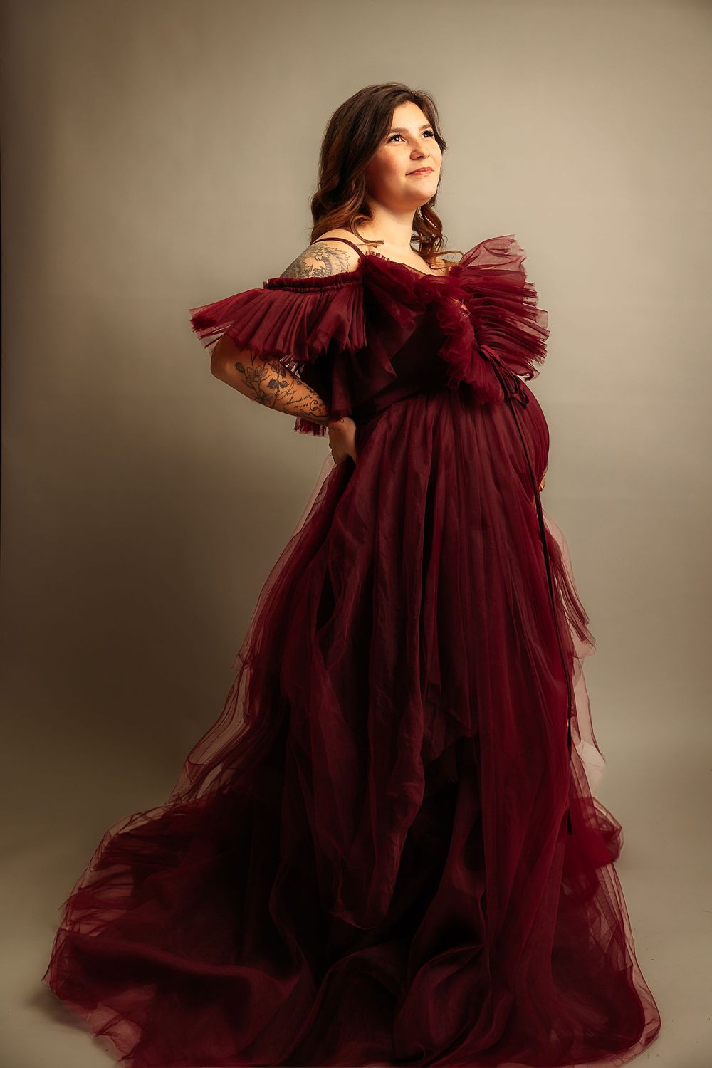 A flowing burgundy tulle maternity gown creates dramatic movement in a studio photoshoot.