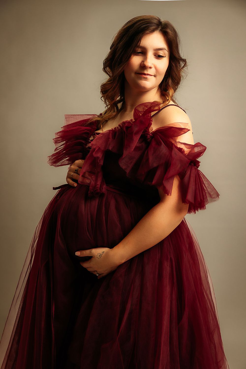 Artistic maternity portraits featuring a dramatic burgundy tulle dress with ruffled details.