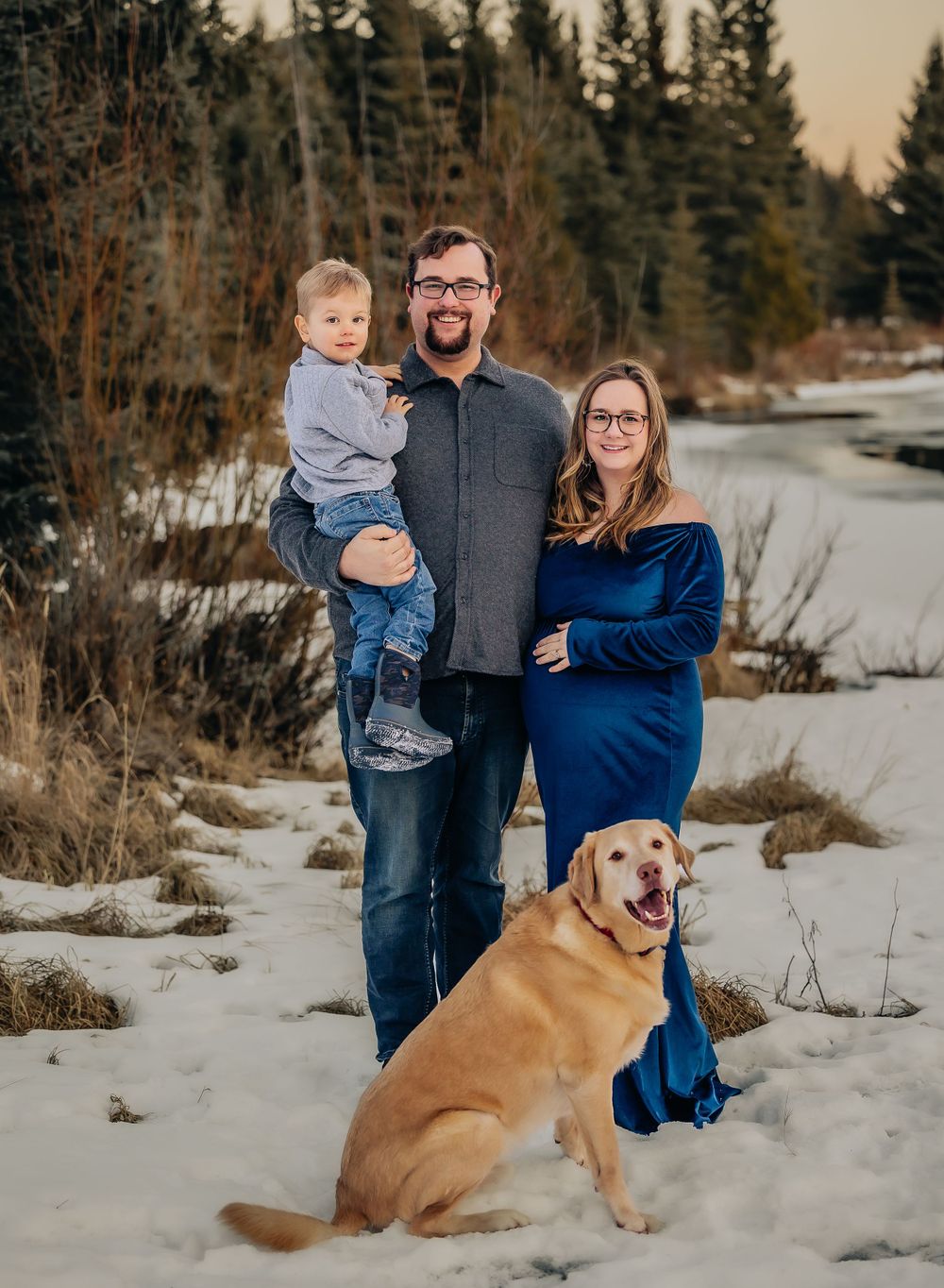 A family portrait in a snowy winter setting with a golden retriever dog sitting in the foreground.