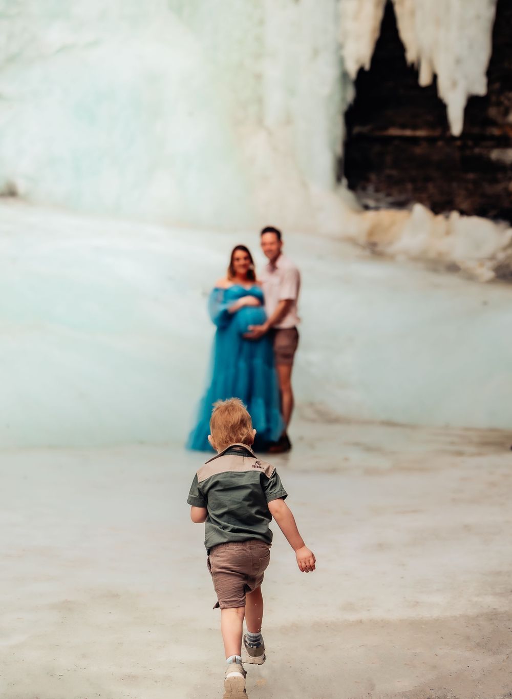 A small child runs towards adults posing in front of a frozen ice wall.