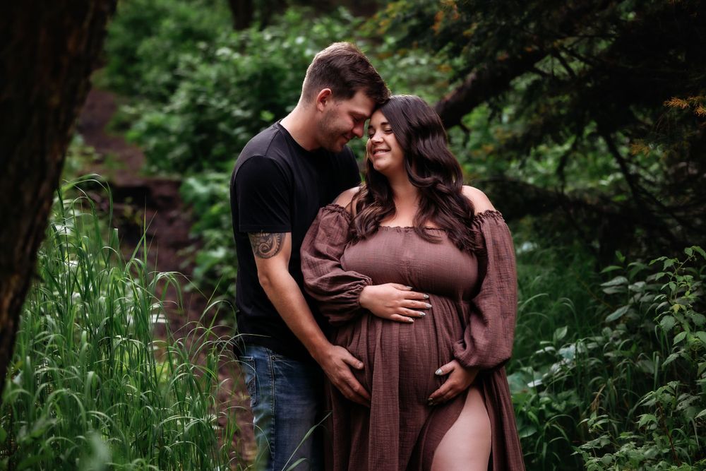 Romantic maternity portrait of couple among lush forest greenery.
