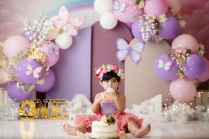 Dreamy first birthday scene with pink and purple balloon arch, butterflies, and floral accents.