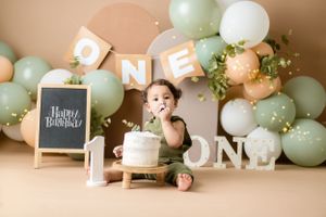 A small child enjoys cake during a first birthday celebration with balloon arch and party decorations.