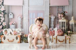 Child sitting in white chair surrounded by pink floral decorations and vintage props.