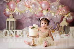 Elegant pink and gold first birthday setup with lanterns, balloons, and decorative cake display.