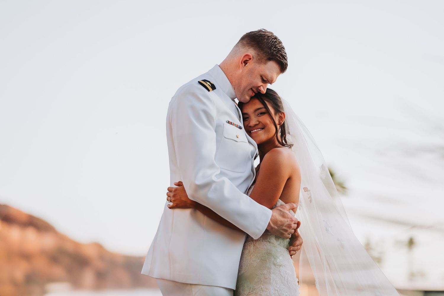 A romantic couple in formal attire holding hands in a desert landscape at sunset.