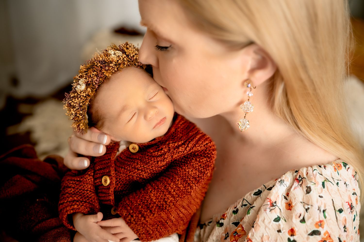 Tender moment between mother and sleeping newborn wearing floral crown.