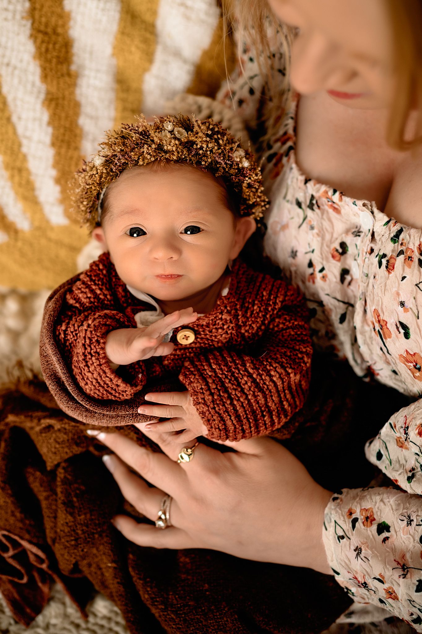 Baby wearing knit burgundy sweater and gold crown headpiece rests on soft yellow blanket.