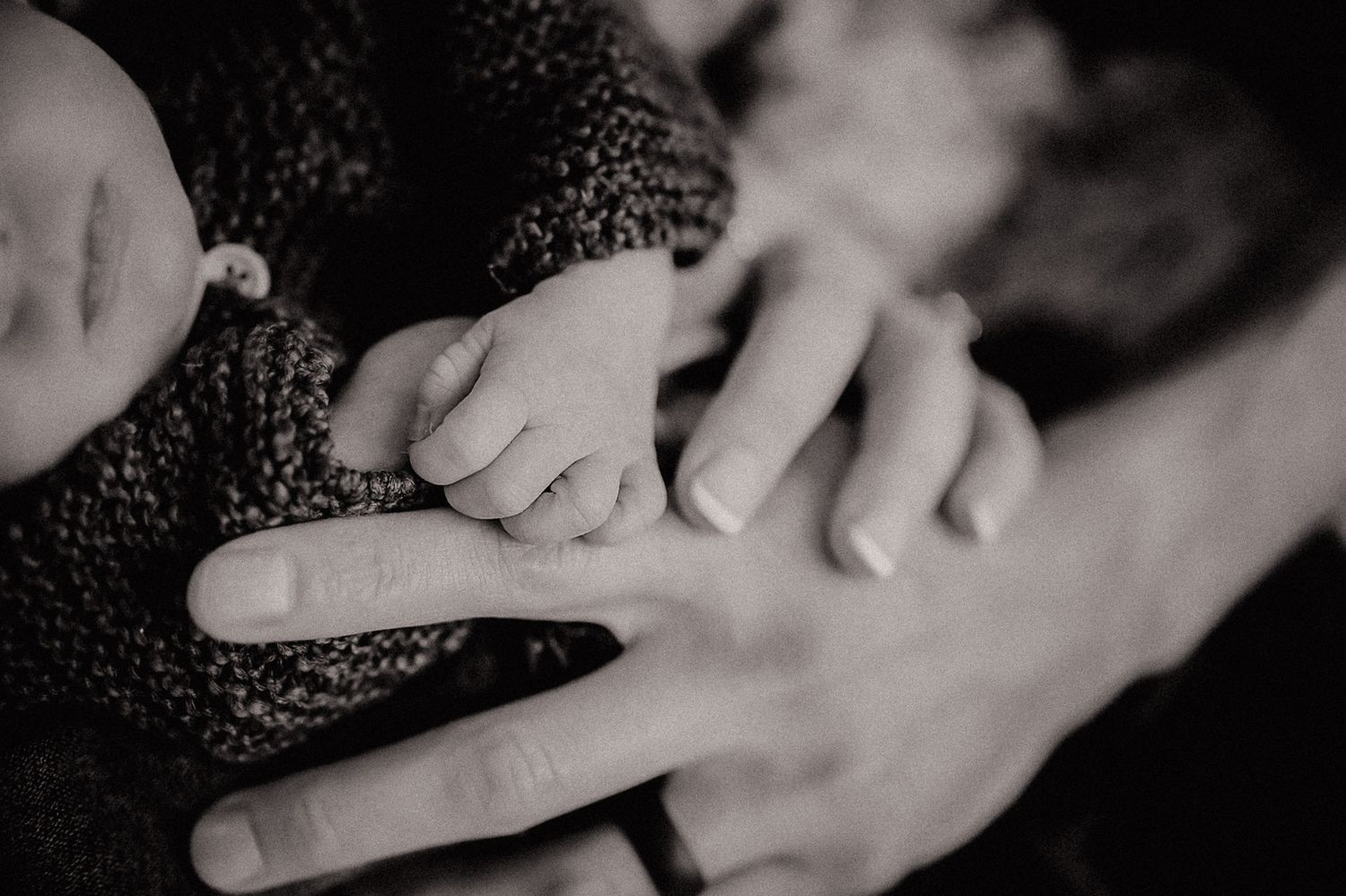 Black and white close-up of tiny infant hand grasping adult finger.