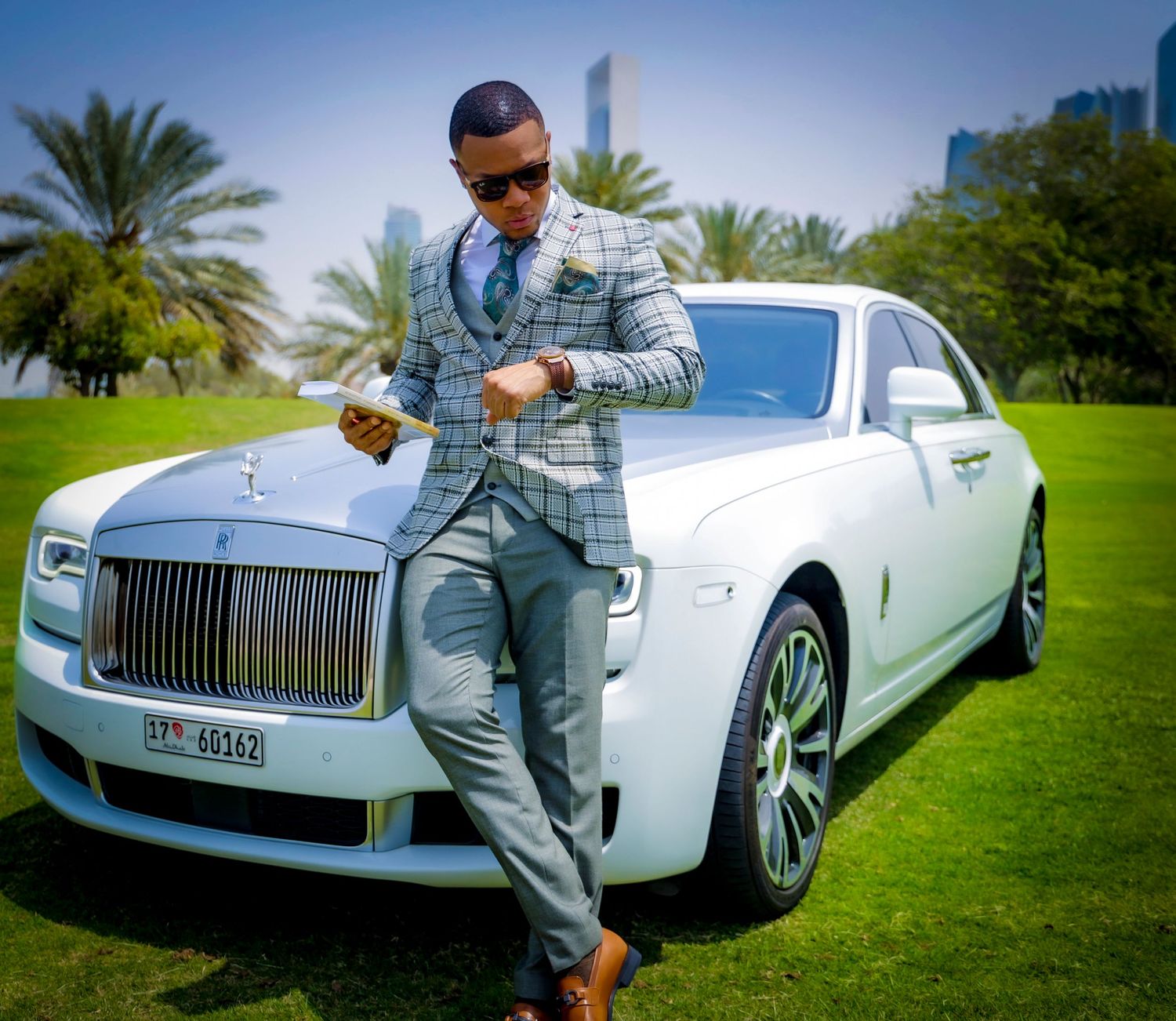 Luxury white Rolls Royce parked on manicured lawn with palm trees.