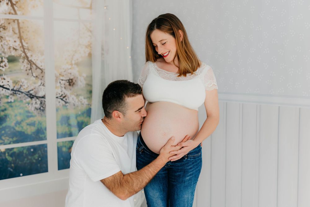 Mujer embarazada y su pareja posando juntos en un estudio fotográfico con fondo neutro y decoración minimalista