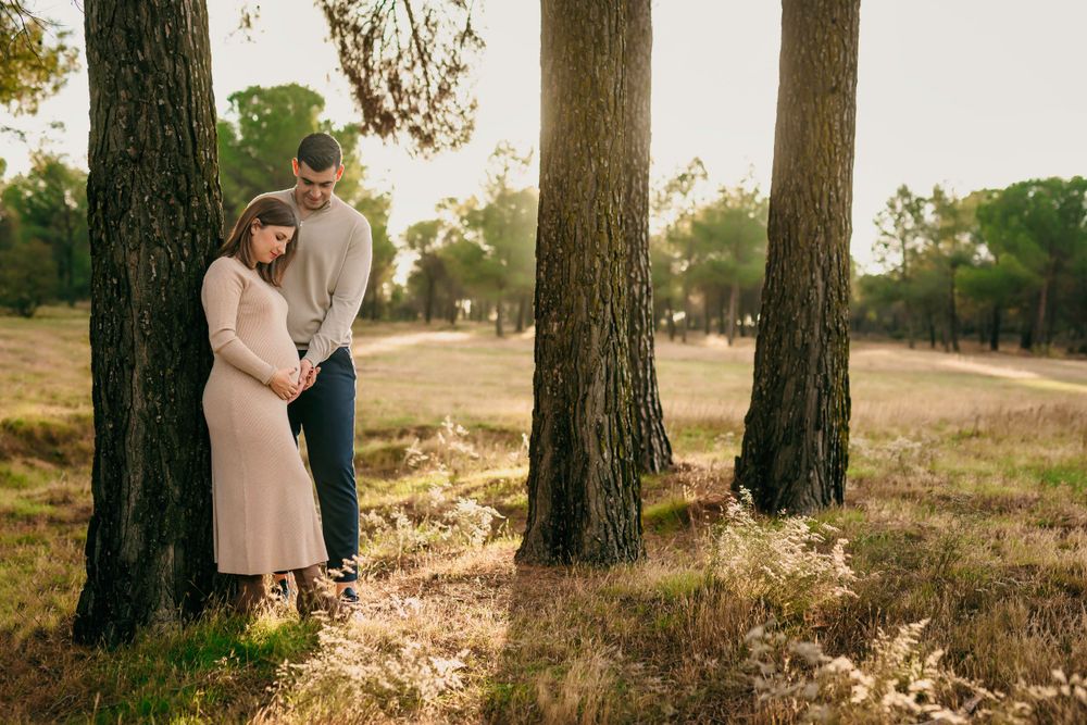 Mujer embarazada y su pareja posando en un paisaje exterior con luz natural durante una sesión de fotos.