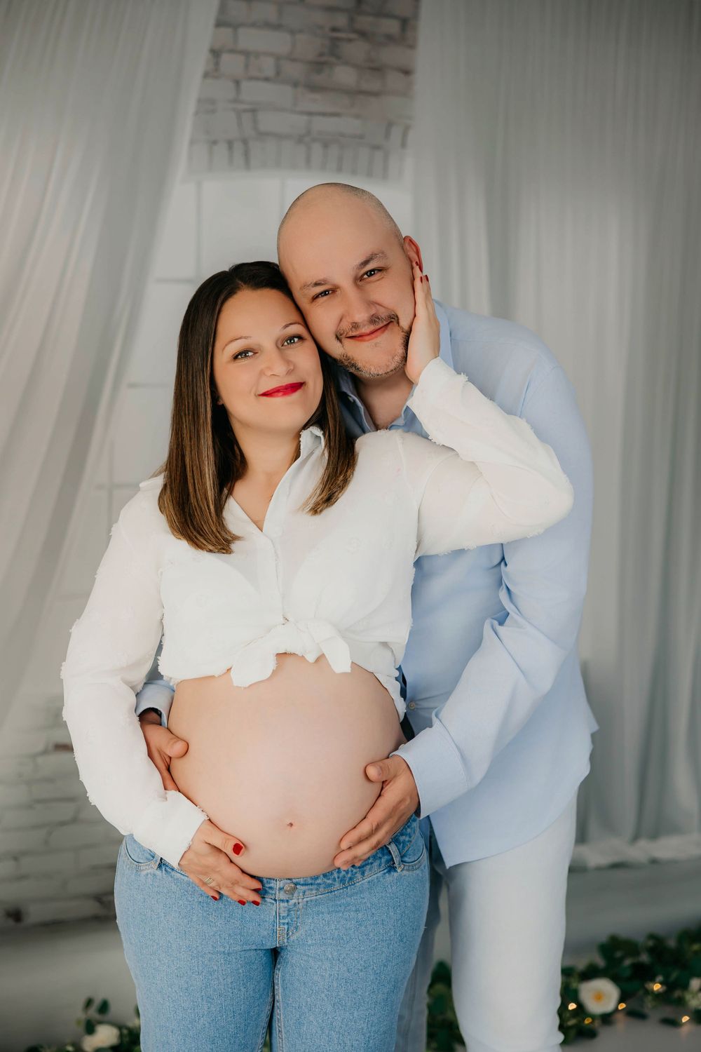 Mujer embarazada y su pareja posando juntos en un estudio fotográfico con fondo neutro y decoración minimalista