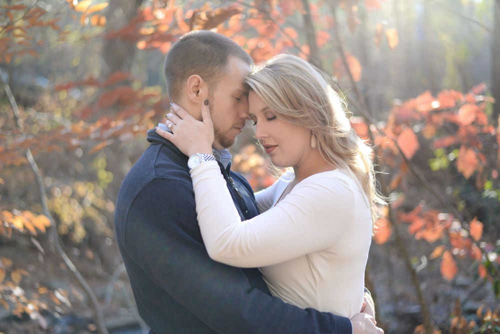A couple embraces in soft autumn light with colorful fall foliage.