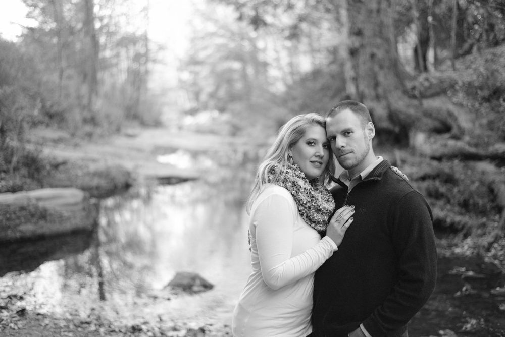 A romantic black and white portrait by a serene stream in the woods.