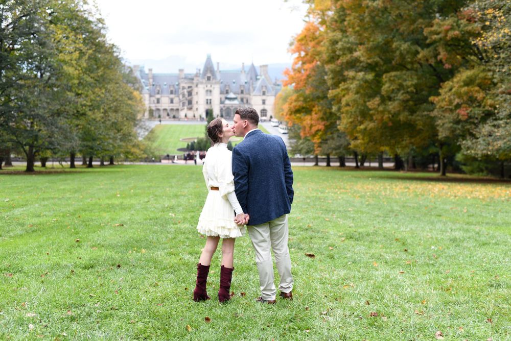 Couple standing together on castle grounds surrounded by autumn trees.