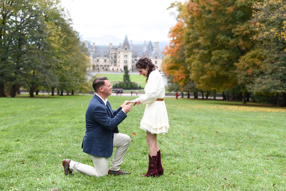 Romantic proposal scene on a grassy lawn with historic castle in the background during autumn.