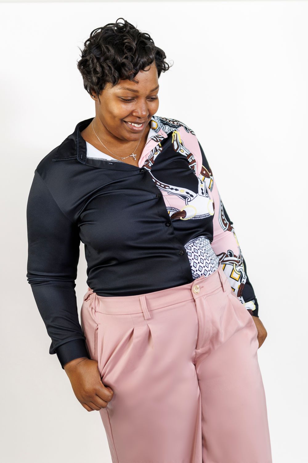 Confident pose in black and floral top paired with pink trousers.