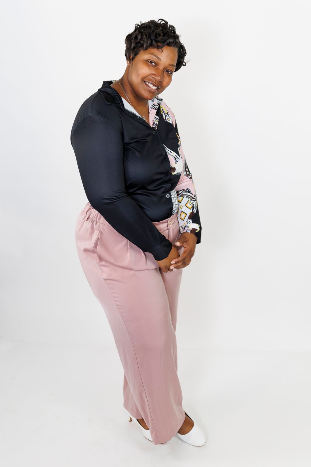 Stylish outfit featuring black top with floral accent and pink pants against white backdrop.