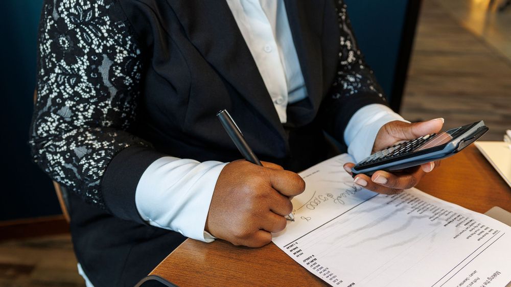 Close-up of hands writing on documents while holding calculator.