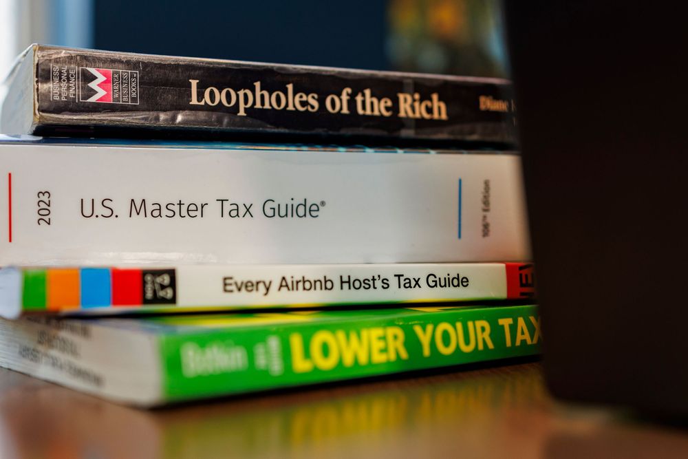 Stack of tax guide books including 'Loopholes of the Rich' and 'Master Tax Guide'.