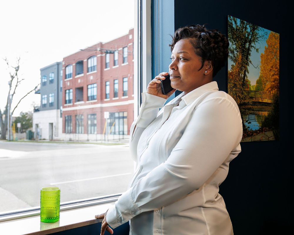 Person in white attire gazing out window while holding green drink.