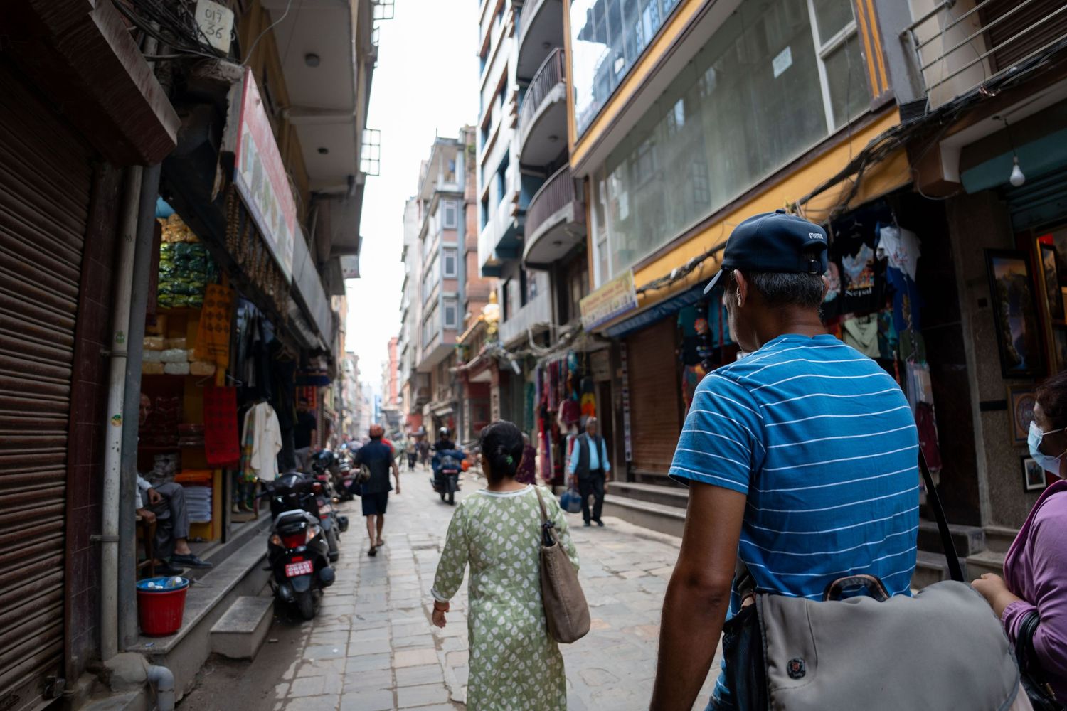 Narrow street scene in Nepal with shops and pedestrians walking along the sidewalk.