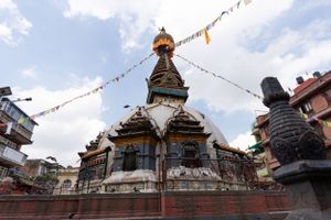 Buddhist temple stupa with colorful prayer flags against a cloudy sky in Nepal.