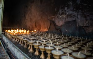 Rows of lit butter lamps create a glowing display inside a Buddhist temple.