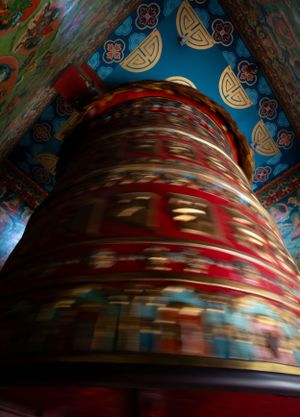 Large prayer wheel with ornate decorative patterns inside a Buddhist temple.