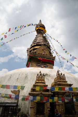 White Buddhist stupa adorned with colorful prayer flags under cloudy skies.