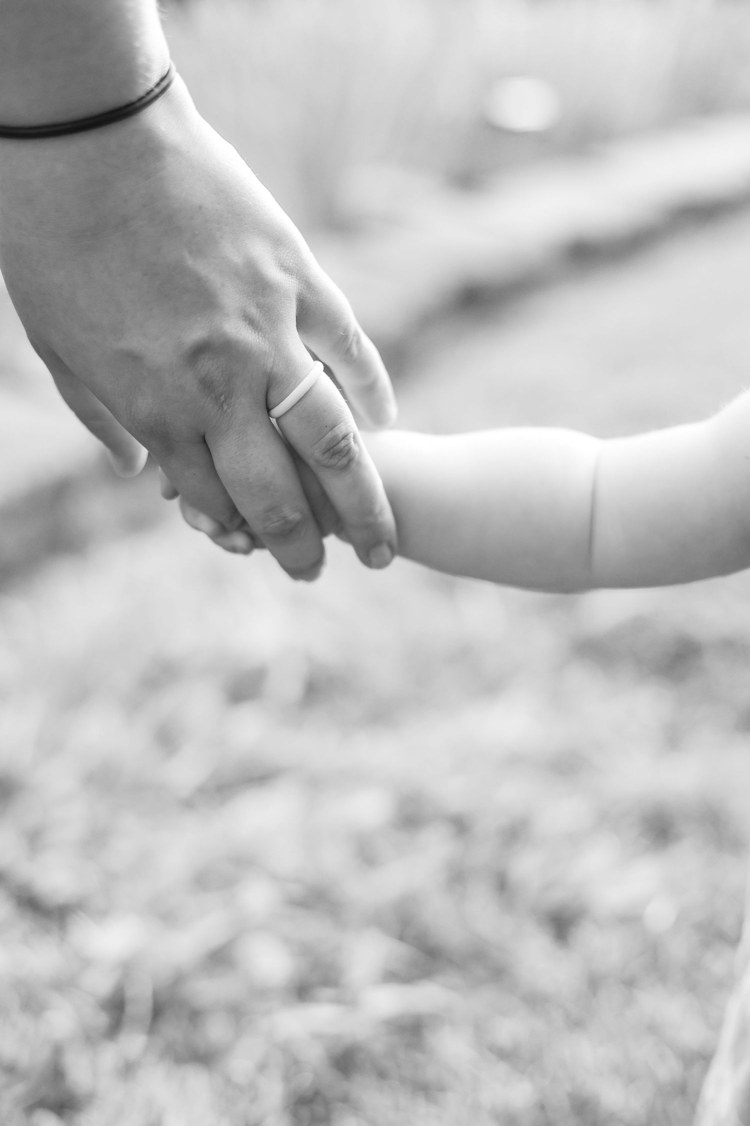 Close-up black and white photo of adult and baby hands touching.